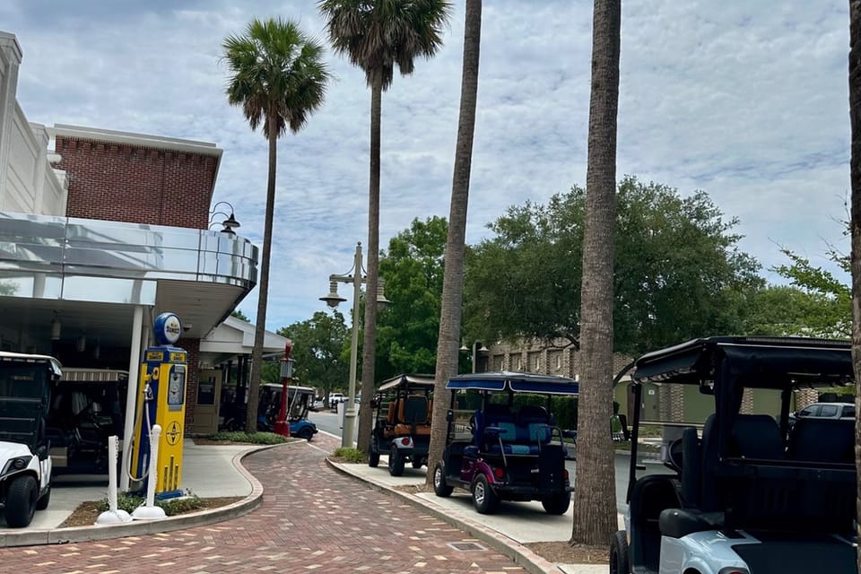 A charming Florida town street lined with tall palm trees, where golf carts serve as the primary mode of transportation alongside a retro-style gas pump station.