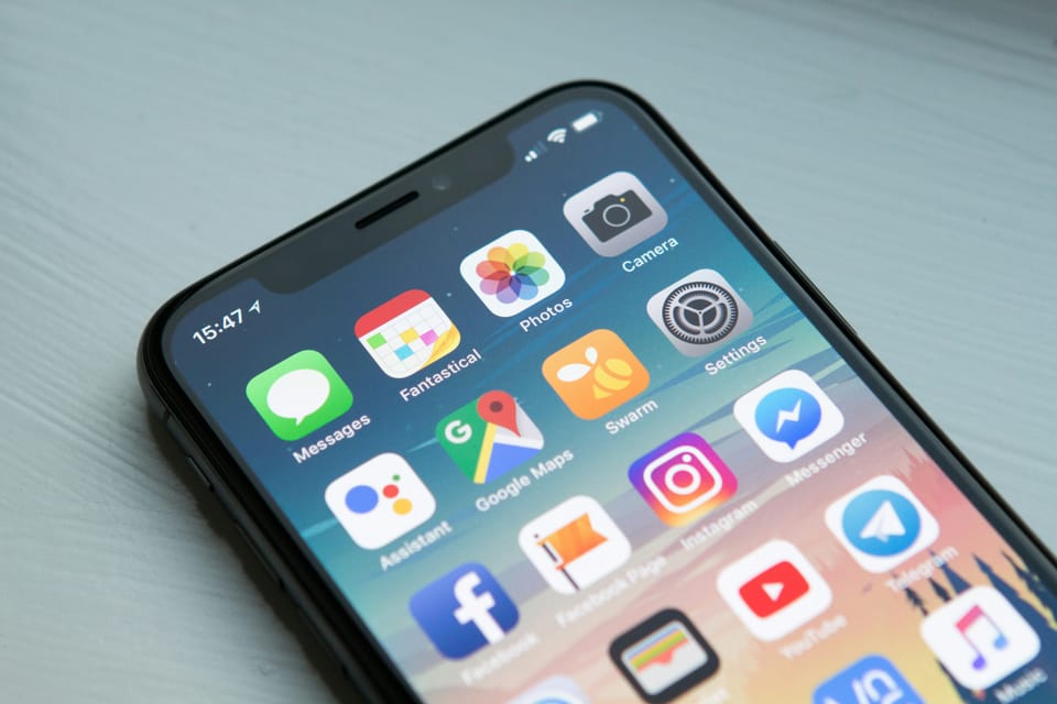 A smartphone lying on a light surface displays a colorful home screen filled with familiar app icons.